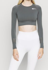 Top corto de manga larga gris con textura acanalada y detalles de malla en las mangas, combinado con leggings blancos de cintura alta.