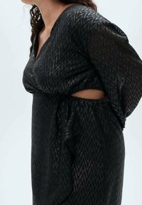Czarna sukienka w wzory z dekoltem w kształcie litery V i wycięciem w talii. Wykonana z fakturowanej tkaniny, z luźnymi rękawami i drapowanym krojem.