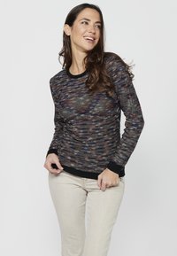 Pull en maille dans un fil multicolore avec un motif texturé, poignets et encolure côtelés noirs. Porté avec un pantalon beige clair.