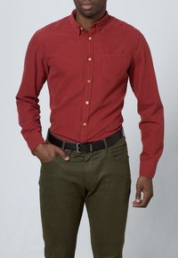 Red long-sleeve button-up shirt with a collar, single chest pocket, and wooden buttons, paired with olive green pants and a black belt.