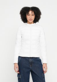 Fehér szigetelt dzseki függőleges steppelt panelekkel, álló gallérral és teljes hosszúságú elülső cipzárral. Simább textúra, testre szabott kialakítás és hosszú ujjú.