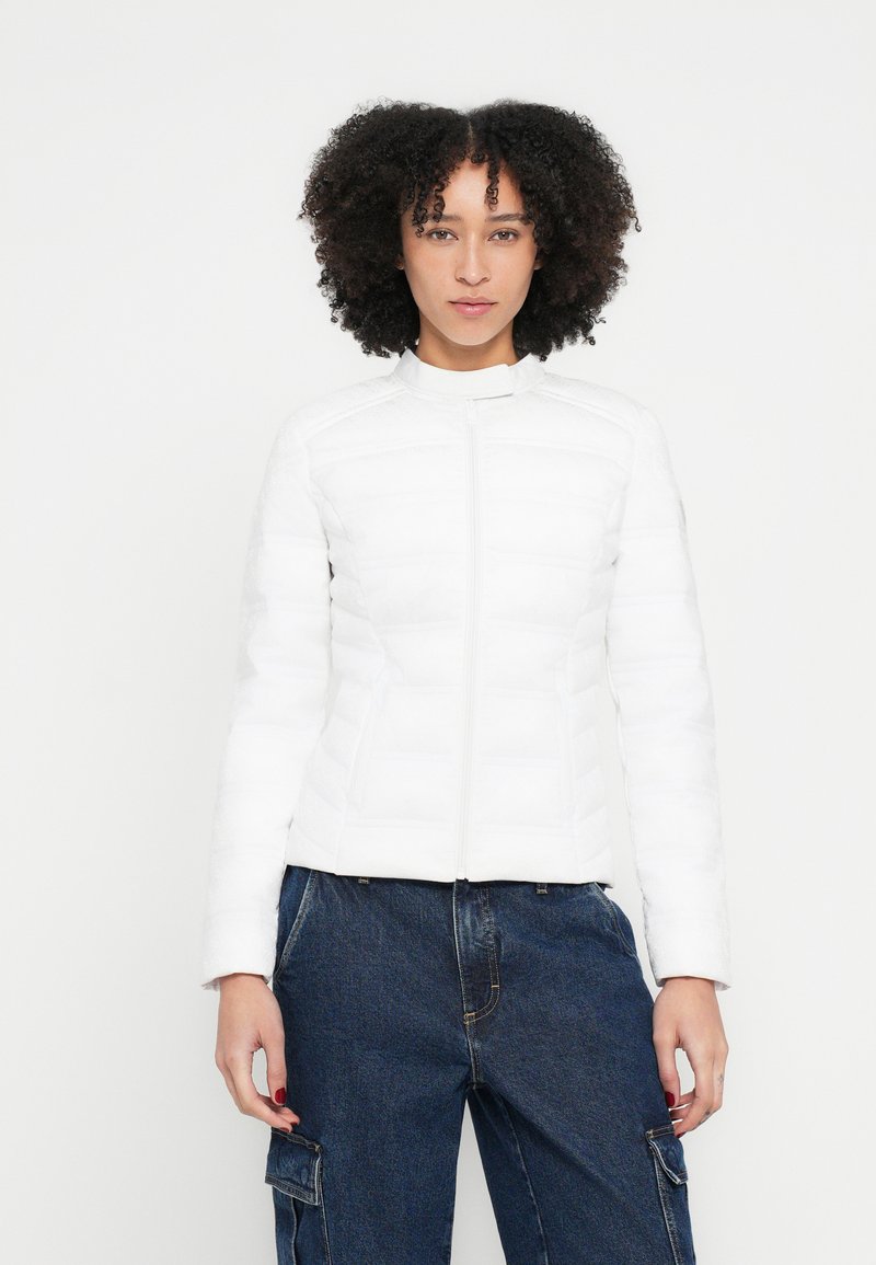 Fehér szigetelt dzseki függőleges steppelt panelekkel, álló gallérral és teljes hosszúságú elülső cipzárral. Simább textúra, testre szabott kialakítás és hosszú ujjú.