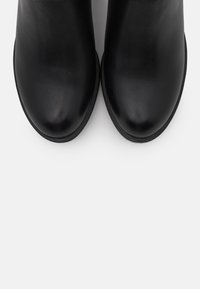 Botas de tobillo de cuero negro con un acabado suave, puntera redondeada y un diseño minimalista, que cuentan con una suela plana y sin herrajes visibles.