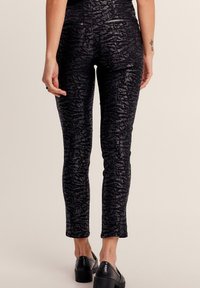 Pantaloni neri attillati con un motivo testurizzato, dotati di tasche posteriori e una finitura lucida. Taglio slim con orlo cropped.