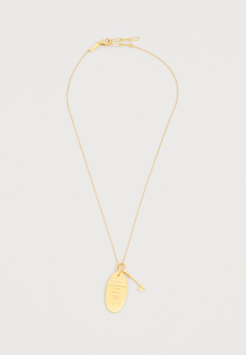 Λεπτό χρυσό κολιέ με αλυσίδα, με οβάλ ταμπελάκι όπου είναι χαραγμένο "COUVENT SAINT MICHEL ACADEMY 98" και μικρό κλειδί ως γούρι κρεμασμένο δίπλα του.