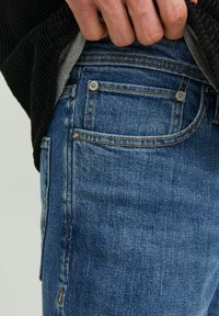 Keskse halli denim teksad, millel on viie tasku disain, kontrastsete helepruunide õmbluste ja metallist nupud taskutel.