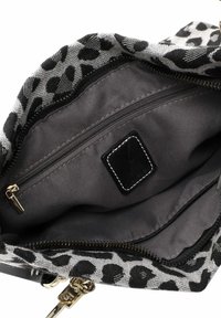 Interno di una borsa a tracolla con stampa leopardata nera e grigia, dotata di una tasca con zip e foderata in tessuto liscio. Presente un hardware dorato distintivo e un'etichetta nera.