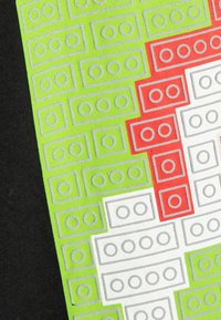 Helle grüne Stoff mit weißen, roten und grauen Blockmustern. Das Design zeigt strukturierte Linien und kreisförmige Formen, die Legosteine ähneln.