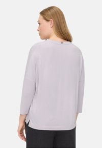 Licht lavendelkleurige blouse met lange mouwen en een ontspannen pasvorm. Heeft een ronde halslijn, zijsplitten en een subtiel detail aan de achterkant van de hals.