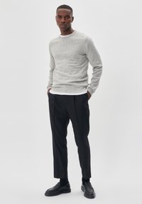 Sivi pleteni pulover s okruglim izrezom, uparen s krojenim crnim hlačama i crnim mokasinkama. Jednostavan dizajn, glatka tekstura i prilagođen oblik.