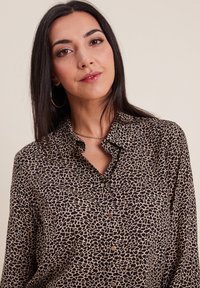 Chemise à boutons imprimée léopard en marron et beige, avec un col et des manches longues, fabriquée dans un tissu léger et doux.