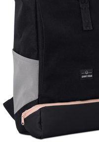 Sac à dos noir avec panneau latéral gris et détails de fermeture éclair rose. Fabriqué en tissu durable, présentant une forme rectangulaire et une étiquette de marque.