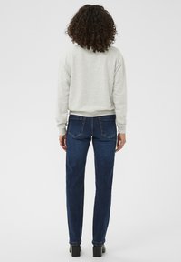 Gaiši pelēks džemperis ar brīvu piegriezumu, valkāts kopā ar tumši ziliem taisnajiem biksēm. Ievērojamas detaļas ietver vienkāršās šuves un divas aizmugurējās kabatas.