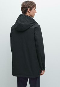 Schwarze Kapuzenjacke mit einem schlichten, geraden Design. Verfügt über elastische Bündchen und einen leicht längeren hinteren Saum. Strukturierter Stoff, keine sichtbaren Muster.
