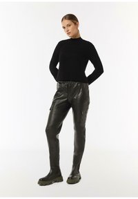 Schwarzer, taillierter Pullover mit hohem Kragen, kombiniert mit schmalen schwarzen Lederhosen mit Taschen auf der Seite. Die Modelle tragen schwarze klobige Stiefel.