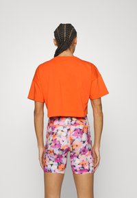Cropped orange t-shirt paired with colorful, floral-patterned shorts. Soft fabric with a relaxed fit, short sleeves, and high waist design.