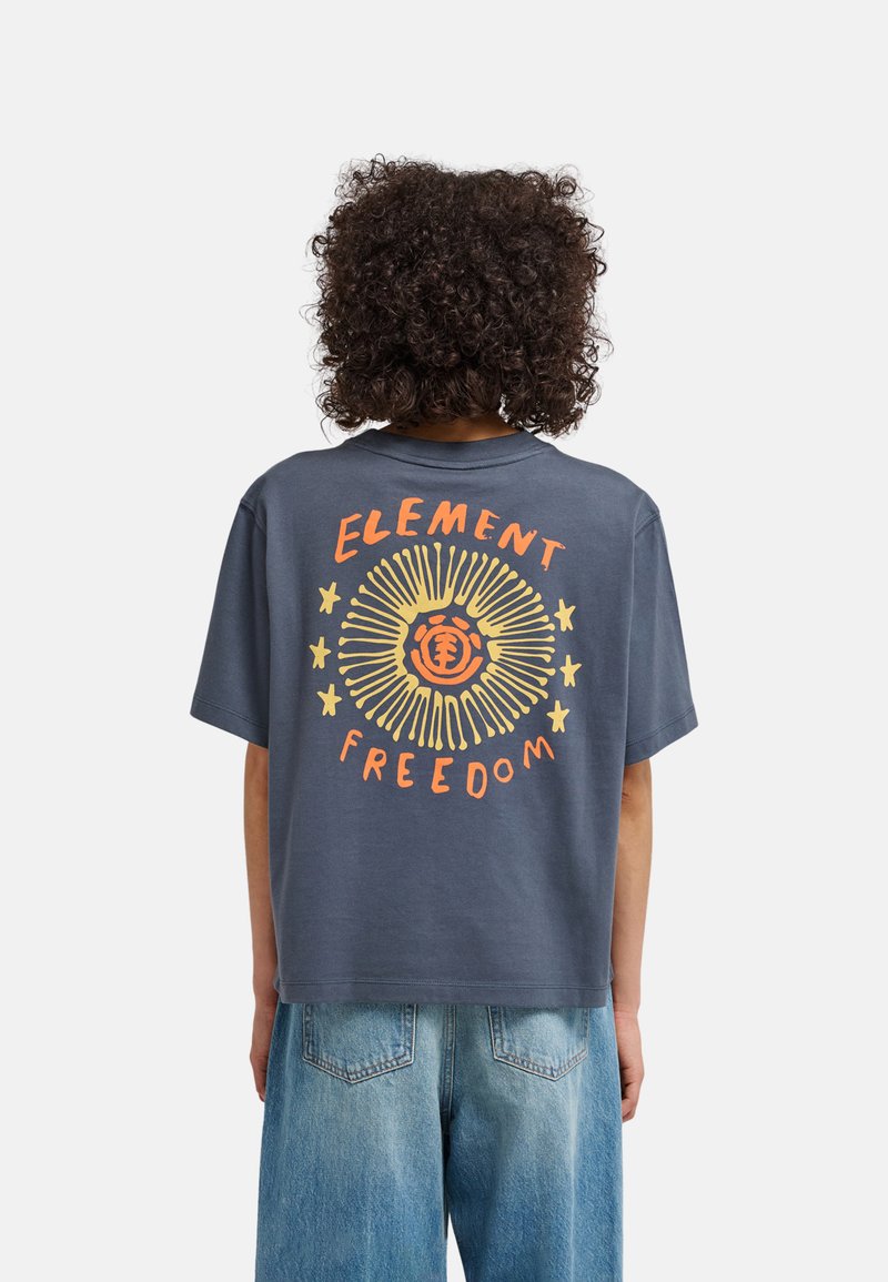 Person with curly hair wearing a dark blue t-shirt with yellow and orange sun and stars graphic and "Element Freedom" text on the back.