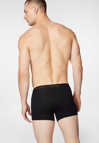 Czarne bokserki męskie o miękkiej teksturze, z jednolitym wzorem i markowym paskiem w talii. Ubranie zakrywa długość do połowy uda.