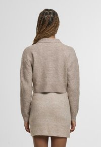 Zestaw swetra i sukienki na szydełku w jasnym beżu, z krótkim swetrem o prążkowanym dole i długimi rękawami, w połączeniu z dopasowaną spódnicą.