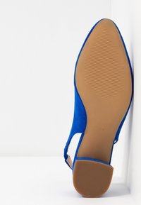 Chaussure à talon haut en daim bleu avec un bout amande et des côtés découpés. La semelle est beige avec des rainures antidérapantes texturées. Taille 37 marquée au-dessous.