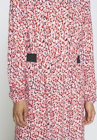 Vestito con motivo rosso e rosa, maniche lunghe, vita stretta e accenti neri ai lati. Tessuto leggero con una texture morbida.