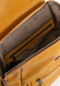 Geel leren tas interieur met een gladde textuur, voorzien van een ritsvak en een aparte sleuf voor organisatie. Rijke bruine voering.