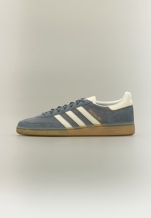 Baskets basses Adidas Spezial en daim bleu avec des bandes blanches, languette de talon beige et semelle en gomme, présentées en profil latéral sur un fond neutre.