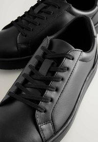 Zwarte leren sneakers met een gladde textuur, ronde vorm, gestikte details en platte zwarte veters over de tong.