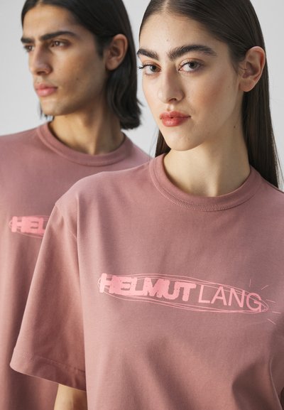 Pink cotton t-shirts with short sleeves, featuring a bold "HELMutLANG" logo in a lighter shade. Smooth texture, casual fit.