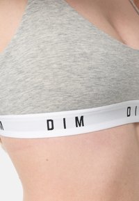 Bralette grigia in cotone con una texture morbida e liscia. Presenta una banda bianca con lettering nero "DIM". Spalline regolabili sono attaccate sul retro.
