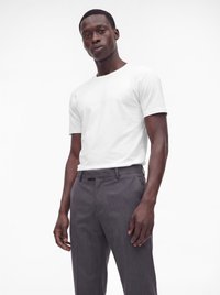 Mann trägt ein einfarbiges weißes Kurzarm-T-Shirt und dunkelgraue Anzughose, steht vor einem weißen Hintergrund.