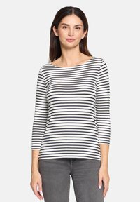 Gestreiftes Langarmshirt in Weiß und Marineblau, mit weitem Kragen und lockerer Passform, aus weichem Stoff gefertigt. Kombiniert mit grauen Hosen.