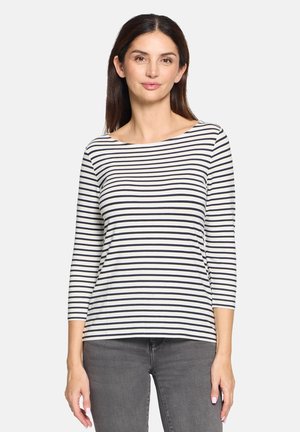 Gestreiftes Langarmshirt in Weiß und Marineblau, mit weitem Kragen und lockerer Passform, aus weichem Stoff gefertigt. Kombiniert mit grauen Hosen.