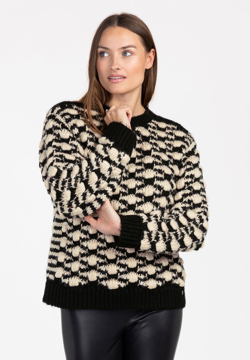 Zwart en crèmekleurig gebreid sweater met een textuur in het breiwerk, ronde halslijn en geribbelde manchetten en onderkant. Het materiaal lijkt dik en gezellig.