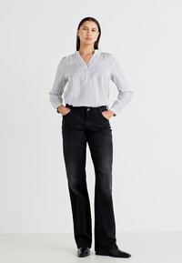 Witte blouse met lange mouwen en verticale blauwe strepen, gecombineerd met zwarte flared jeans. De jeans hebben een vijf-pocket ontwerp en een middelhoge taille.