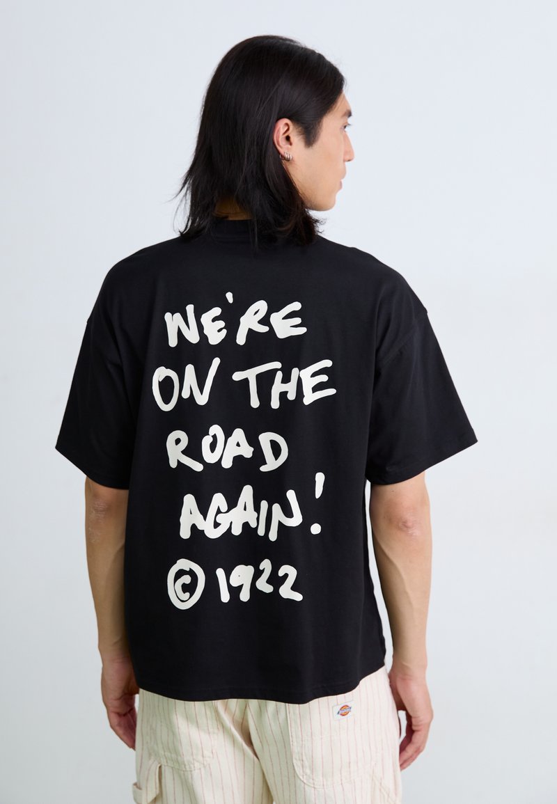 T-shirt en coton noir avec un grand texte blanc au dos indiquant « NOUS SOMMES DE RETOUR SUR LA ROUTE ! » avec ©1922, coupe surdimensionnée et manches courtes.