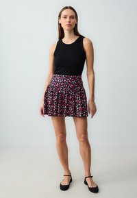Schwarzes ärmelloses Oberteil kombiniert mit einem ausgestellten Minirock mit pink-weißer Blumenmusterung, ergänzt durch schwarze Schuhe.
