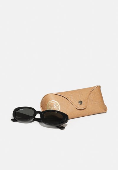 Lunettes de soleil noires avec des montures rondes, posées à côté d'un étui beige en texture, avec un logo doré "Ray-Ban" et une fermeture à pression.