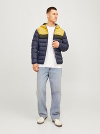 Mėlynas ir geltonas pūkinis džemperis su kapišonu, su užtrauktuku priekyje, spalvų blokų dizainu ir horizontaliais siūlais. Dėvimas ant baltos marškinėlių.