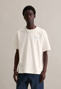 Korte mouwen, crèmekleurig katoenen T-shirt met een losse pasvorm, voorzien van blauwe tekst op de borst en een ronde halslijn.