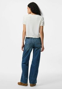 Vit kortärmad cropped t-shirt i kombination med högmidjade, löst sittande blå jeans och bruna slip-on skor. Minimalistisk design, utan mönster.