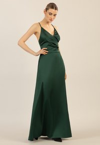 Ein langes, smaragdgrünes Satin-Kleid mit V-Ausschnitt und drapiertem Oberteil, dünnen Trägern und fließender Form, glatter Textur und einem dezenten Glanz.