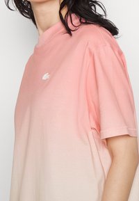 T-shirt ombré rose en coton doux avec un col rond. Il présente un petit logo blanc sur la poitrine et des manches courtes avec une coupe décontractée.