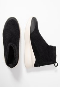 Černé slip-on tenisky s chlupatým vrškem, ko�ženými akcenty a silnou krémově zbarvenou podrážkou. Mají poutko na patě pro snadné obouvání.