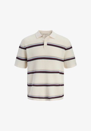 Ragazzo che indossa un cappellino rosso, una polo a maniche corte a righe, pantaloncini di denim verdastri, calzini bianchi e scarpe beige, che guarda di lato.