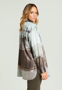 Luźna koszula z długim rękawem w jasnoniebieskich i ciemnobrązowych odcieniach, zdobiona nadrukiem krajobrazu. Miękki materiał o gładkiej fakturze z zaokrąglonym dołem.