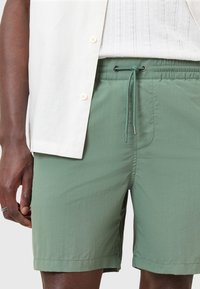 Pantaloni da bagno verdi, leggeri, con vita elastica, chiusura con cordoncino e tasche laterali. Tessuto strutturato, design fino al ginocchio.
