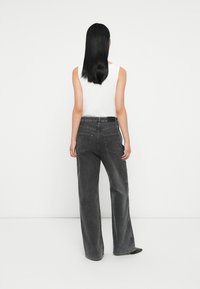 Jean large gris avec taille haute, poches arrière et détails de couture subtils ; associé à un haut sans manches blanc uni.