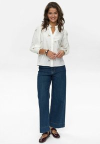 Blusa bianca con ricami floreali, scollatura a V e maniche a sbuffo abbinata a jeans a vita alta blu scuro con gamba larga e ballerine bordeaux.
