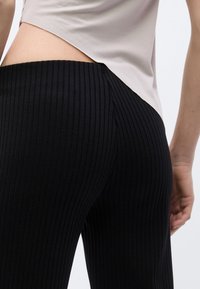 Μαύρο ριμπ κολάν με ψηλή μέση και κομψό σχέδιο, συνδυασμένο με ανοιχτό μπεζ τοπ με διαγώνιο κόψιμο στο τελείωμα.